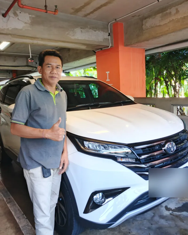 Gede Susrawan giving a thumbs up beside his white Toyota Rush