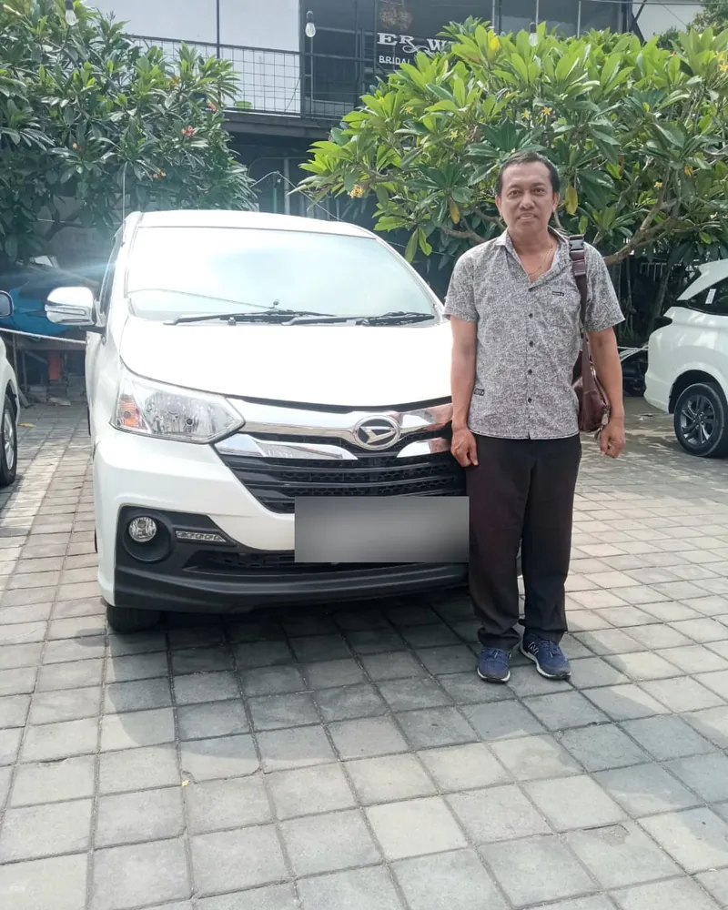 Ngurah Yoga standing beside his white Daihatsu Xenia